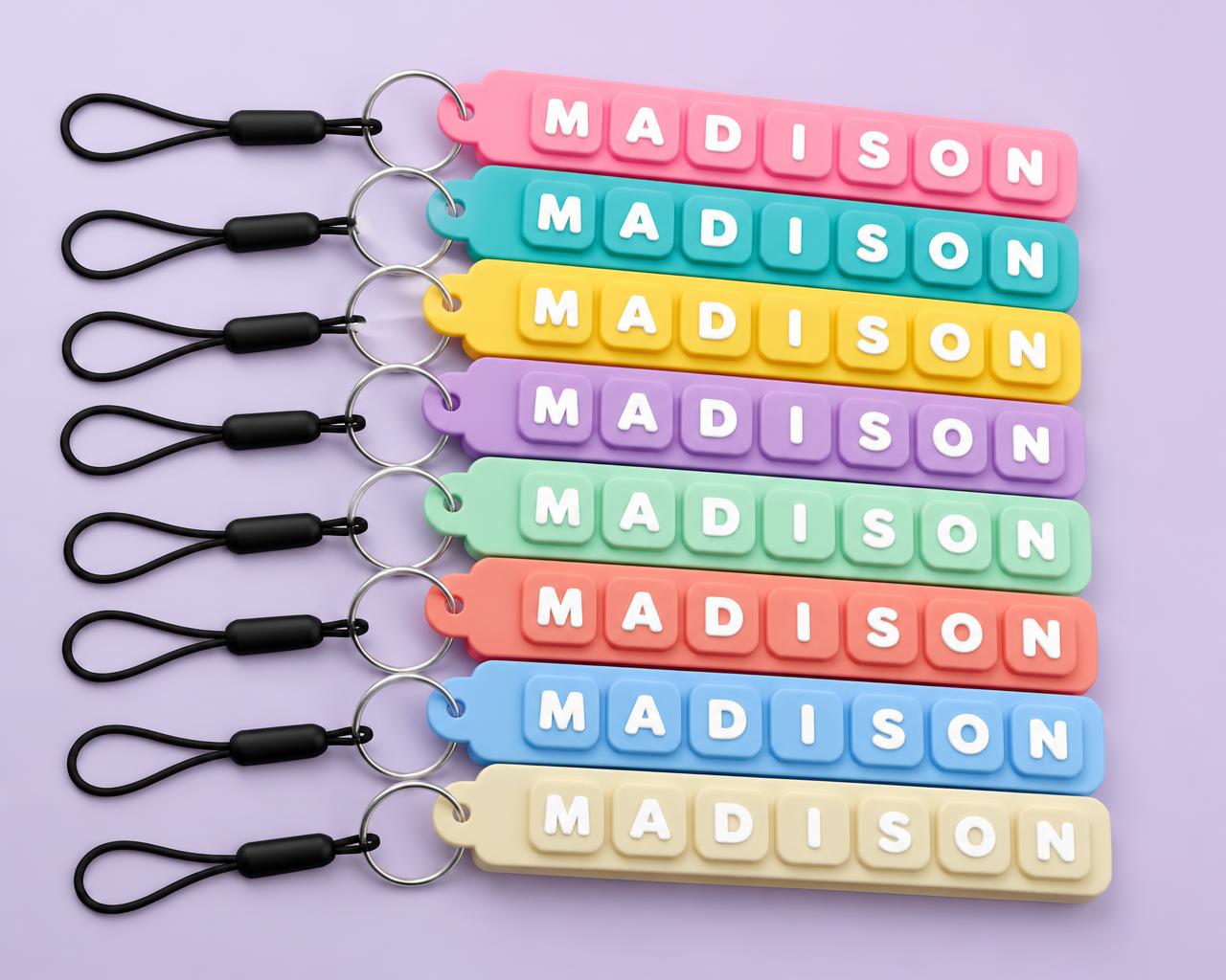Eight name fidget clicker keychains fanned out in pink, turquoise, yellow, lavender, coral, mint, blue and white